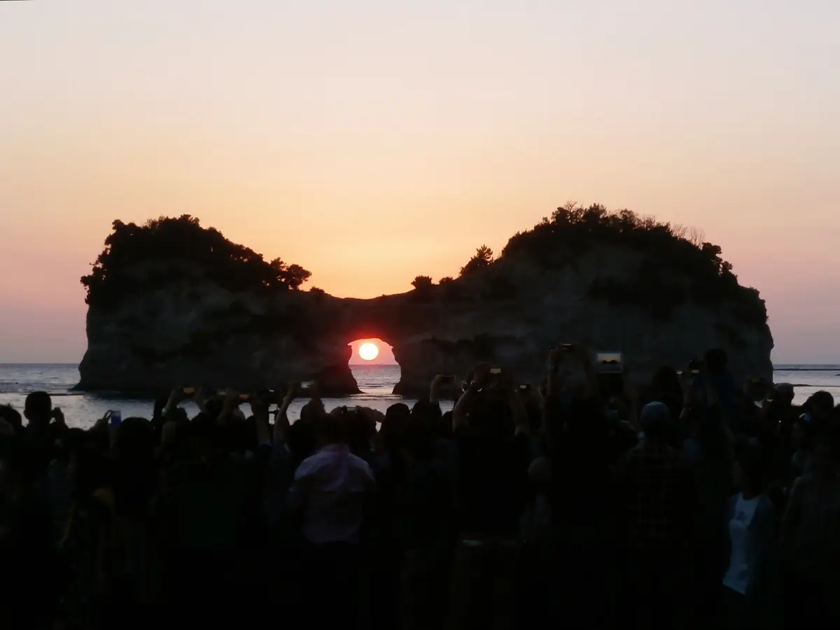 遊客的剪影正在拍攝落進圓月島拱洞的夕陽