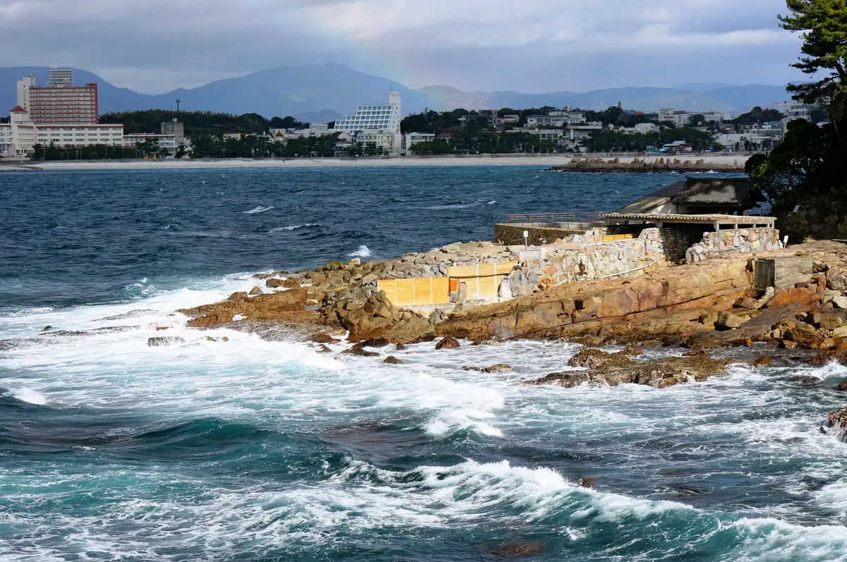 海浪拍打白濱溫泉海邊的岩石，海灣對岸是白良濱的飯店群