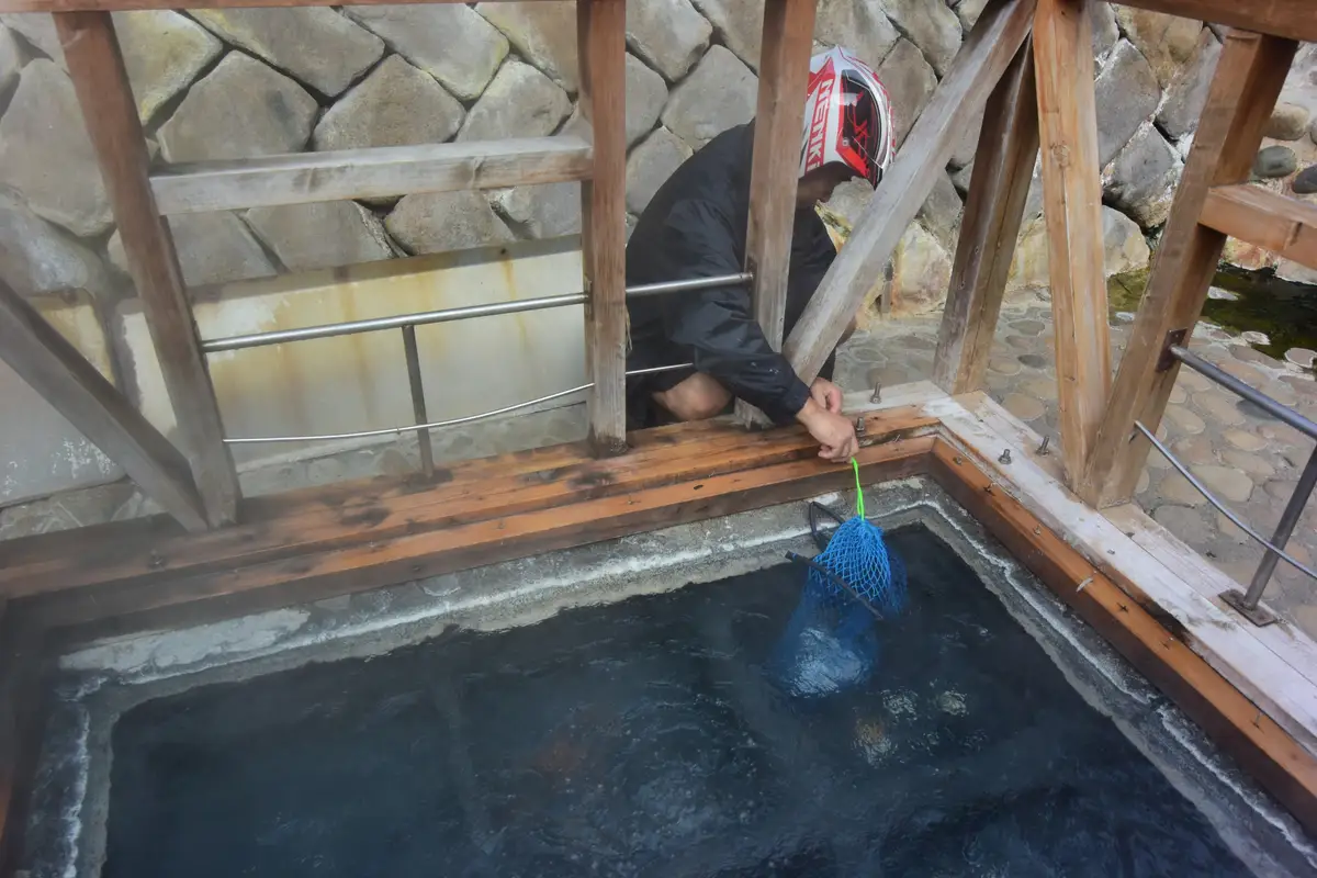湯けむりの上がる湯の峰温泉の湯筒に、網袋に入れた卵を沈める人